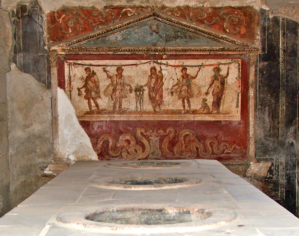 Ancient Roman thermopolium counter with inset serving jars and a painted wall behind it